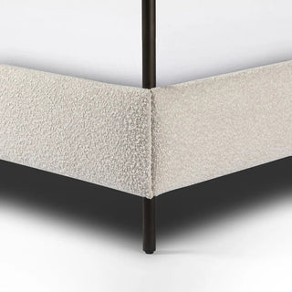 Close-up of the corner of a queen-size canopy bed, showing boucle fabric upholstery and sleek black metal legs.