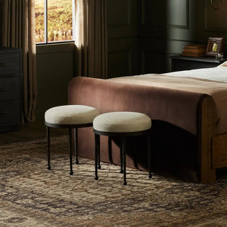 Styled interior setting with two upholstered hammered iron accent stools at the foot of a bed in a moody, modern bedroom.