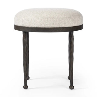 Side view of a midcentury hammered iron accent stool featuring a round cushioned seat and slim legs.