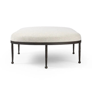 Side profile of a hammered bronze iron cocktail ottoman with a curved upholstered top and delicate iron legs.