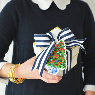 Person holding a decorative Christmas ornament with a blue and white striped bow.