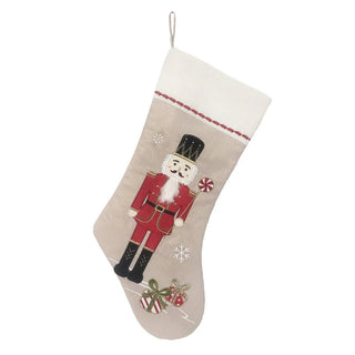 A red and beige Christmas stocking with a nutcracker design, hanging against a white background.